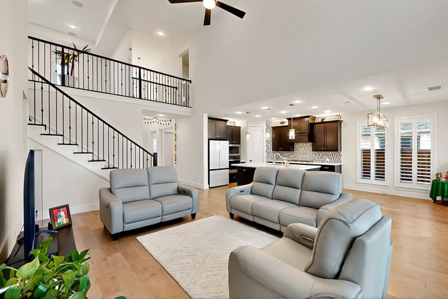 Living area featuring a ceiling fan, light wood finished floors, a towering ceiling, stairway, and baseboards | Image 8