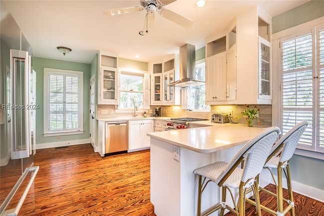 Kitchen with light hardwood / wood-style floors, backsplash, white cabinets, dishwasher, and exhaust hood | Image 21