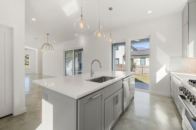 Kitchen with range, concrete flooring, a sink, and stainless steel dishwasher | Image 14