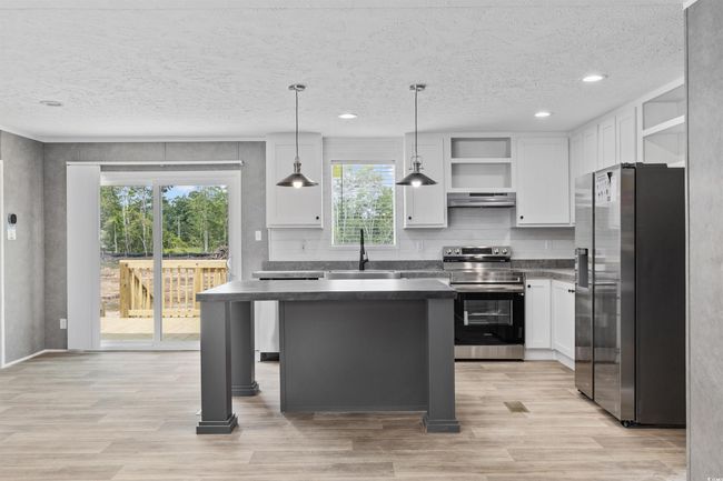 Kitchen with stainless steel appliances, open shelves, dark countertops, exhaust hood, and light wood-style flooring | Image 12