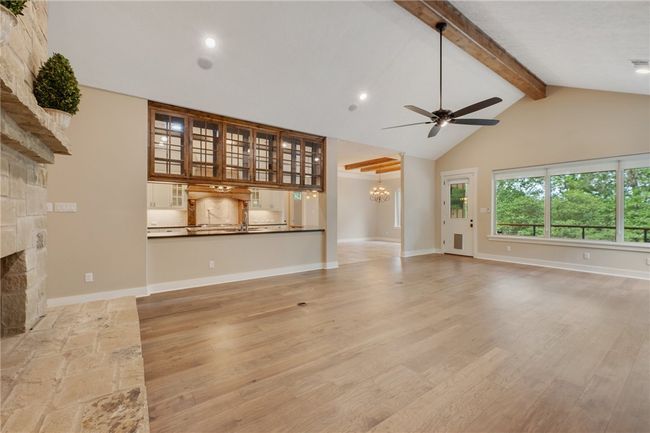 Unfurnished living room featuring beam ceiling, a ceiling fan, light wood-style flooring, high vaulted ceiling, and a stone fireplace | Image 4