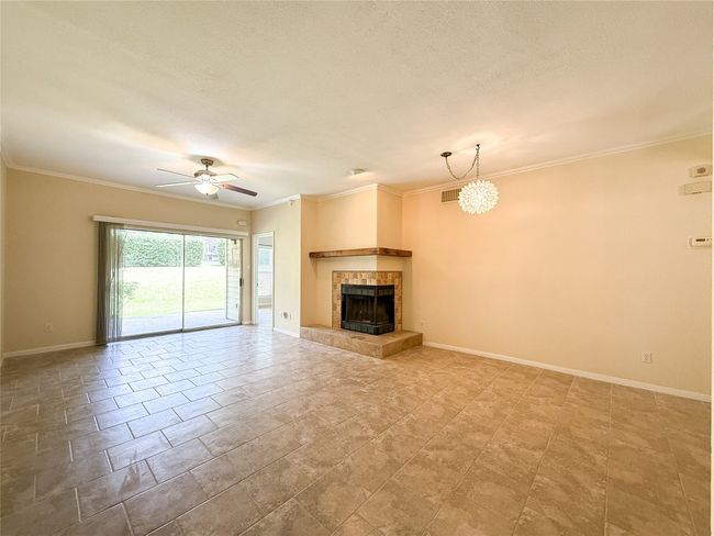 Unfurnished living room with ceiling fan, crown molding, a tiled fireplace, and a chandelier | Image 8