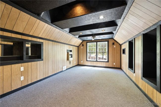 Unfurnished living room featuring visible vents, lofted ceiling, a ceiling fan, wood walls, and carpet floors | Image 32