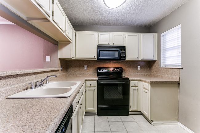 Kitchen featuring black appliances, a textured ceiling, light tile patterned flooring, light countertops, and white cabinetry | Image 13