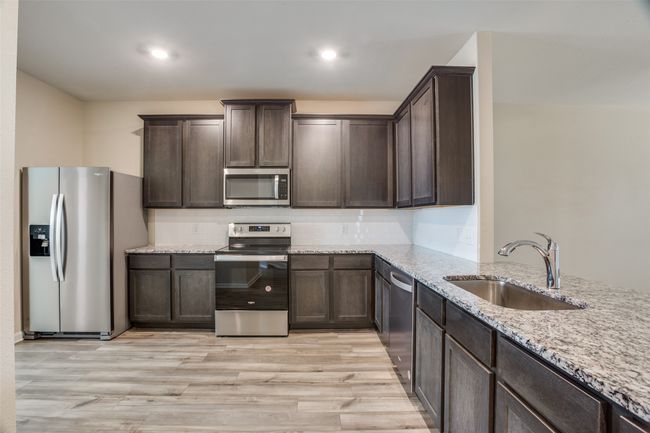 Kitchen featuring a sink, dark brown cabinetry, light wood-style flooring, appliances with stainless steel finishes, and light stone countertops | Image 5