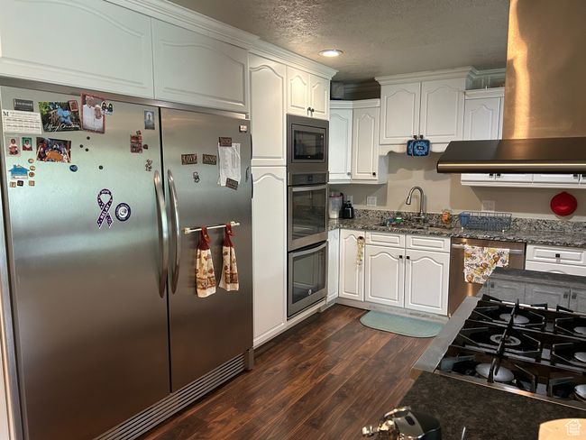 Kitchen with appliances with stainless steel finishes, dark wood-style flooring, a sink, white cabinets, and wall chimney range hood | Image 14