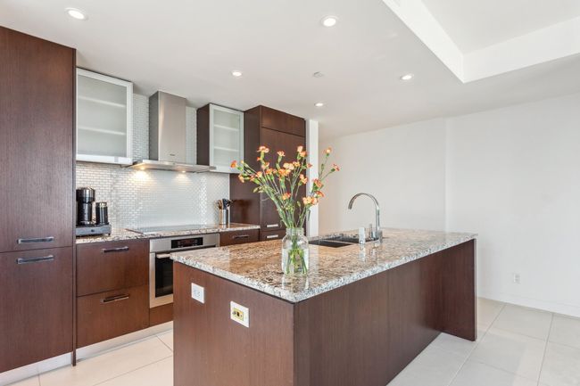 Kitchen featuring decorative backsplash, a sink, wall chimney exhaust hood, stainless steel oven, and a center island with sink | Image 4