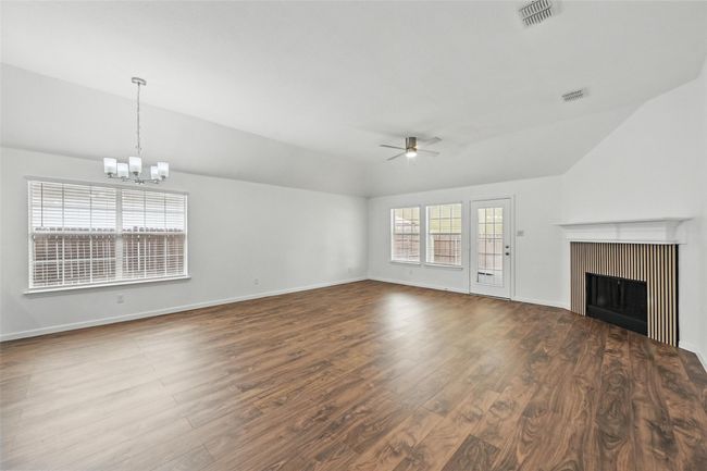 Unfurnished living room featuring a ceiling fan, a chandelier, lofted ceiling, a fireplace, and dark wood-style flooring | Image 19