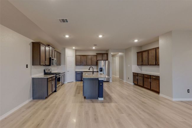 Kitchen with decorative backsplash, light wood-style floors, visible vents, baseboards, and appliances with stainless steel finishes | Image 11