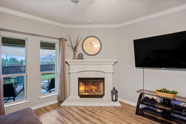 Living room featuring wood finished floors, crown molding, a lit fireplace, and baseboards | Image 5