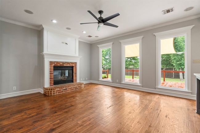 Unfurnished living room featuring wood finished floors, a fireplace, ceiling fan, crown molding, and baseboards | Image 15