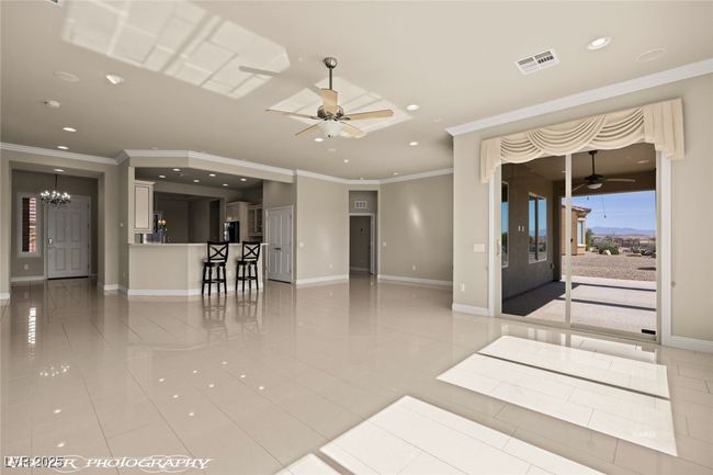 Unfurnished living room featuring baseboards, recessed lighting, crown molding, visible vents, and ceiling fan with notable chandelier | Image 29