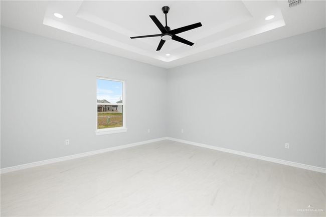 Empty room with a raised ceiling, ceiling fan, recessed lighting, and baseboards | Image 8