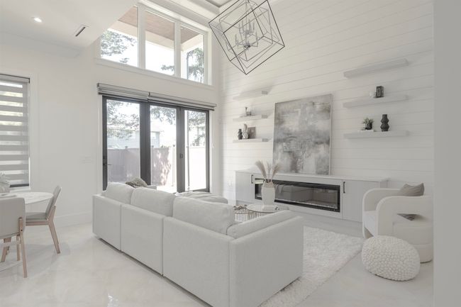 Living area featuring a glass covered fireplace, a high ceiling, a chandelier, baseboards, and wooden walls | Image 11