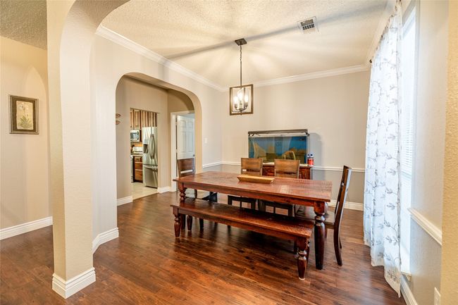 Dining area featuring dark wood finished floors, arched walkways, a textured ceiling, ornamental molding, and a chandelier | Image 6