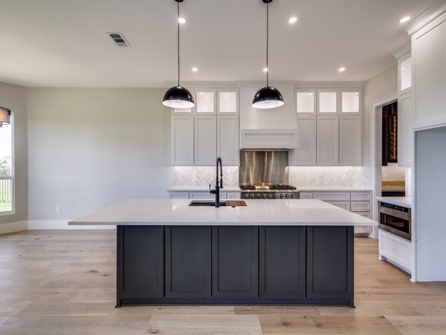 Kitchen with a professional style sink on beautiful center island, elegant herringbone backsplash, white custom cabinetry, professional and recessed lighting | Image 20