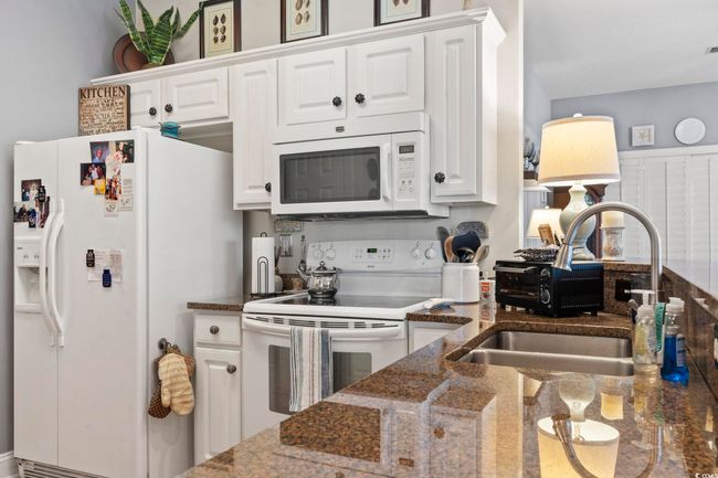 Kitchen with white appliances, white cabinets, dark stone countertops, and a sink | Image 9