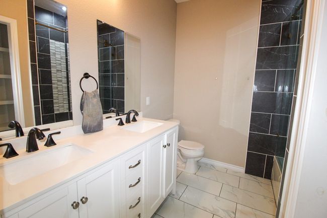 Full bathroom with marble look tiles, double vanity, and tiled bathtub | Image 11