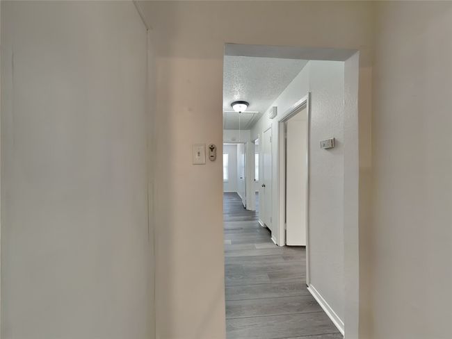 Hall with attic access, a textured ceiling, wood finished floors, and baseboards | Image 4