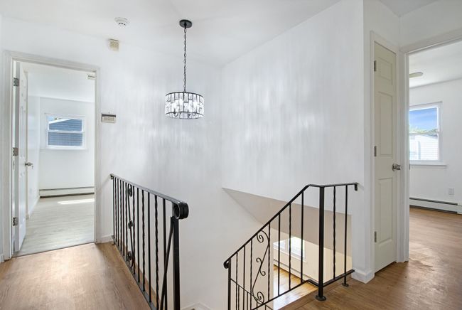 Stairway featuring a baseboard heating unit, wood finished floors, baseboard heating, and a chandelier | Image 18