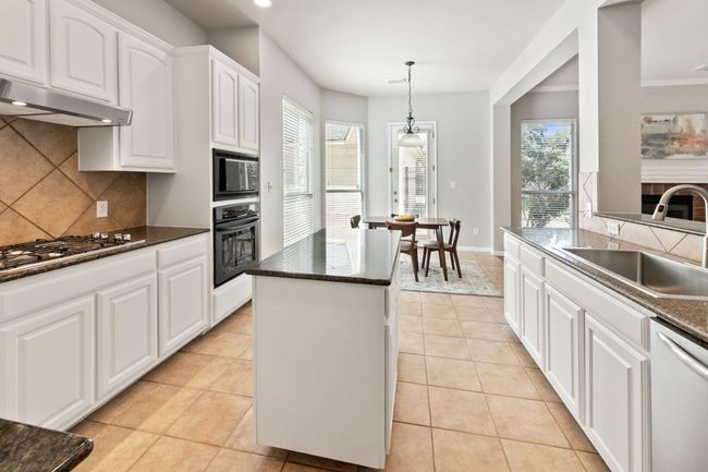 Kitchen featuring black appliances, decorative backsplash, a kitchen island, under cabinet range hood, and white cabinetry | Image 12