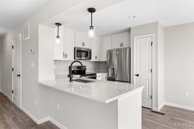 Kitchen with appliances with stainless steel finishes, a peninsula, light stone counters, light wood-style flooring, and recessed lighting | Image 9