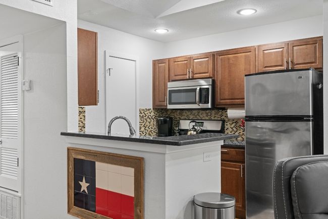 Kitchen with appliances with stainless steel finishes, dark countertops, decorative backsplash, brown cabinets, and a sink | Image 12