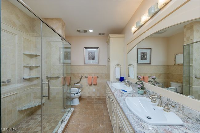 Primary bathroom featuring toilet, tile walls, a sink, and visible vents | Image 32