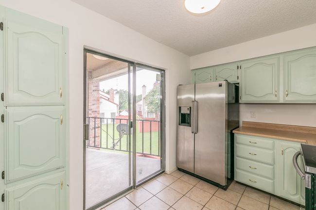 Kitchen with stainless steel fridge with ice dispenser, green cabinets, stove, light tile patterned floors, and a textured ceiling | Image 8