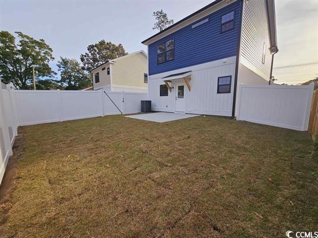 Back of property at dusk featuring a fenced backyard, central air condition unit, a lawn, a gate, and a patio area | Image 22