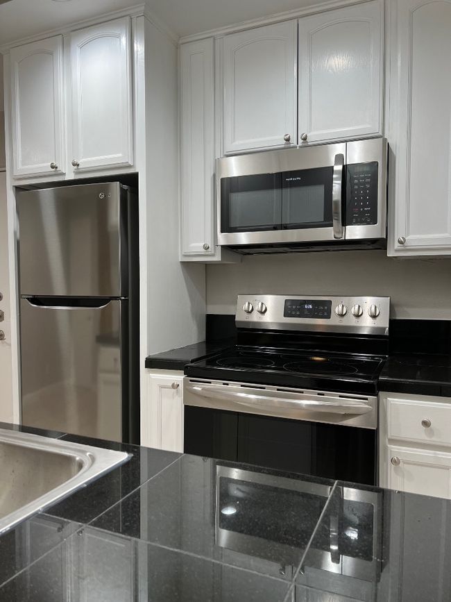 Kitchen with stove, refrigerator, white cabinetry, and dark countertops | Image 4