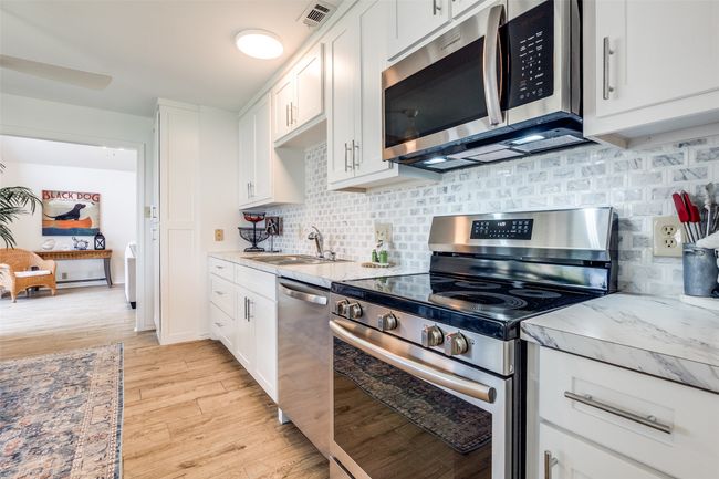 Kitchen featuring appliances with stainless steel finishes, light wood-style flooring, white cabinets, and backsplash | Image 11