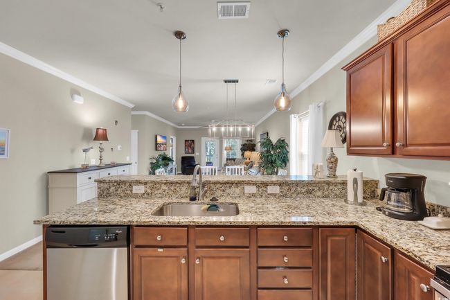 Kitchen with stainless steel dishwasher, crown molding, decorative light fixtures, light stone counters, and a peninsula | Image 9