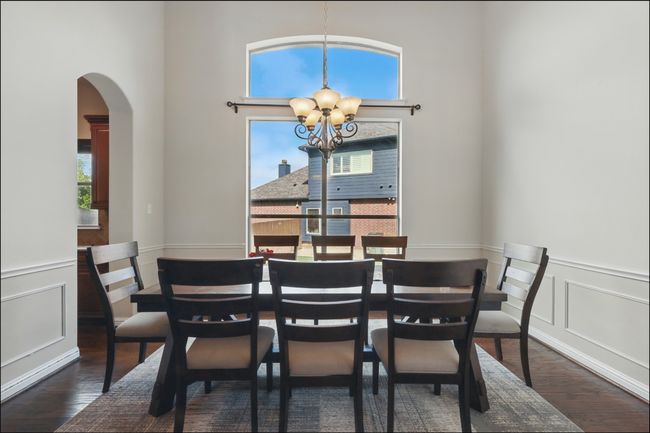 Dining room with wood finished floors, arched walkways, a chandelier, stairs, and a wainscoted wall | Image 7