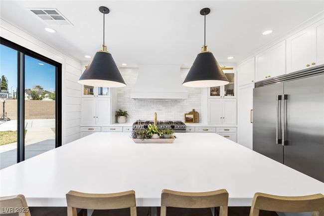 Kitchen featuring custom exhaust hood, stainless steel appliances, light countertops, white cabinetry, and visible vents | Image 13