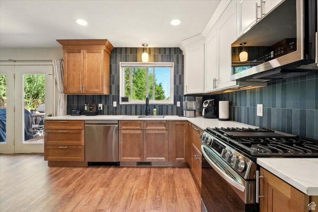Kitchen with appliances with stainless steel finishes, a sink, light countertops, backsplash, and light wood-type flooring | Image 7