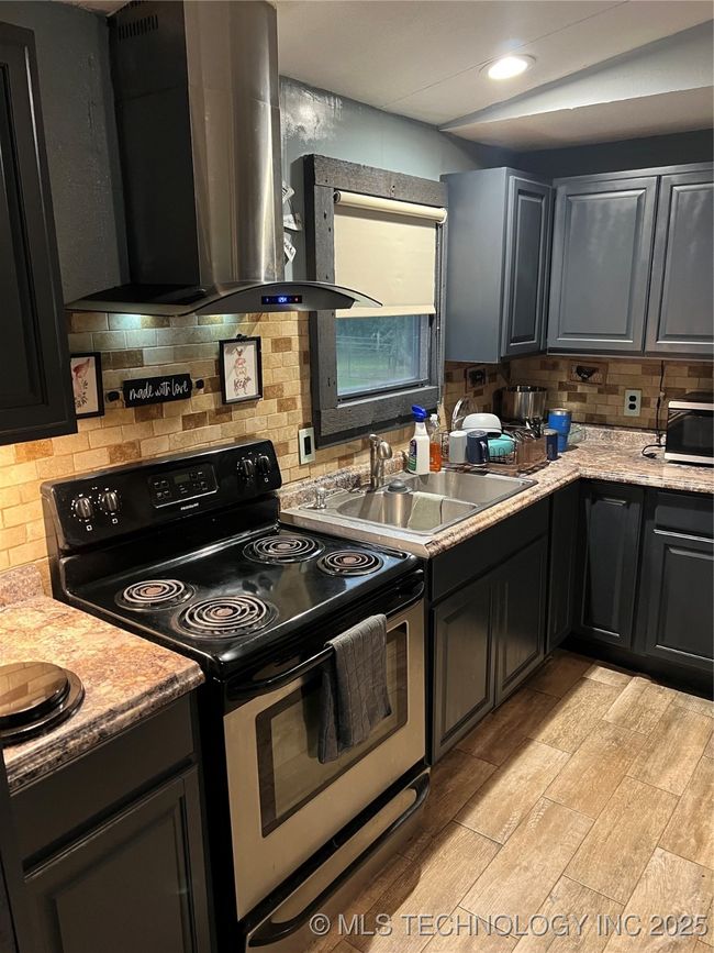 Kitchen featuring stove, ventilation hood, a sink, tasteful backsplash, and light wood-style floors | Image 8