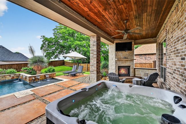 Fenced backyard with an outdoor stone fireplace, a patio, a ceiling fan, and a hot tub | Image 35