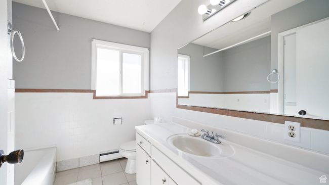 Bathroom with toilet, a bathtub, vanity, a baseboard radiator, and a wainscoted wall | Image 15