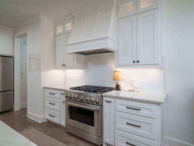 Kitchen featuring appliances with stainless steel finishes, premium range hood, decorative backsplash, dark wood finished floors, and white cabinets | Image 12