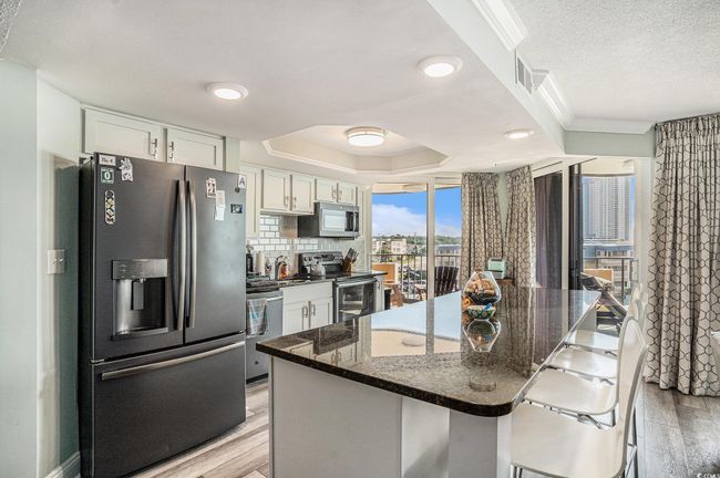 Kitchen featuring appliances with stainless steel finishes, light wood-style floors, white cabinets, a kitchen island, and a tray ceiling | Image 12