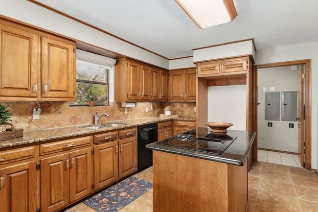 Kitchen with brown cabinetry, black appliances, a center island, a sink, and stone countertops | Image 17