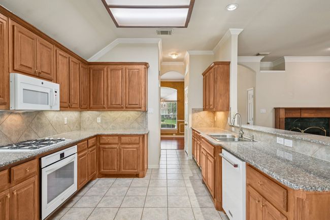 Kitchen with decorative backsplash, a fireplace, brown cabinets, white appliances, and light tile patterned flooring | Image 8