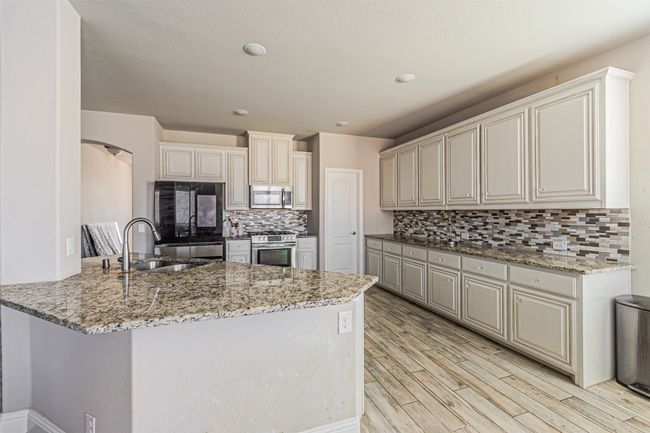 Kitchen featuring appliances with stainless steel finishes, a sink, a peninsula, light stone counters, and tasteful backsplash | Image 11