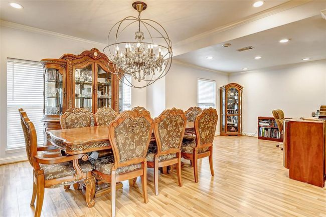 An expansive dining space, positioned just off the entryway, is framed by large windows that brighten the room. A dramatic statement chandelier pairs with recessed lighting, casting a warm glow over the generous layout—perfect for hosting gatherings in style. | Image 6