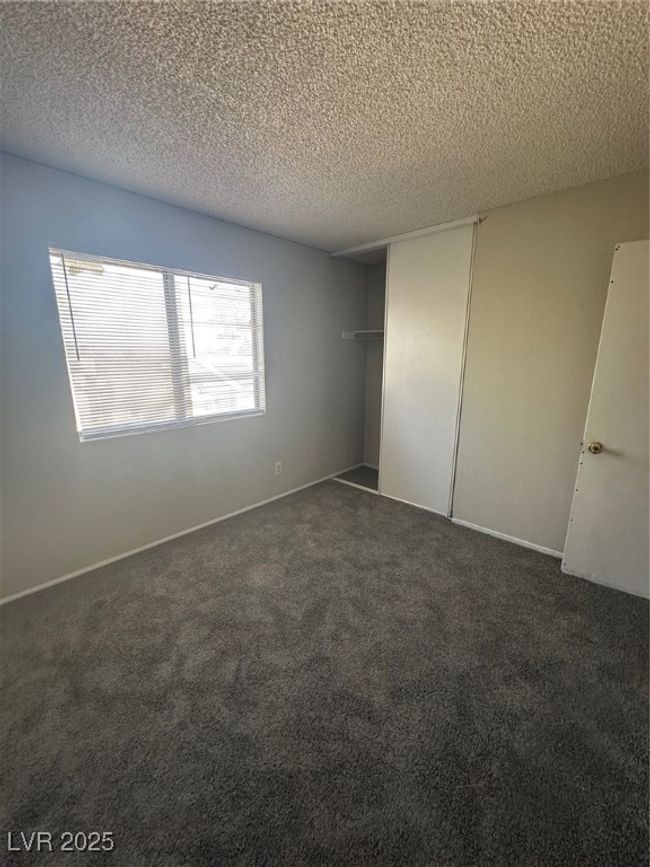 Unfurnished bedroom with a textured ceiling, dark colored carpet, and a closet | Image 11