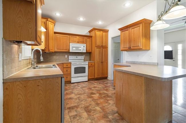 Kitchen with a sink, white appliances, a peninsula, decorative light fixtures, and decorative backsplash | Image 14