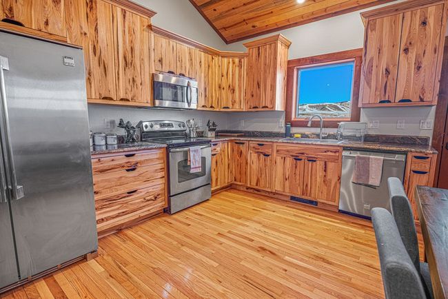 Kitchen featuring light wood-style flooring, a sink, vaulted ceiling, appliances with stainless steel finishes, and dark stone counters | Image 10