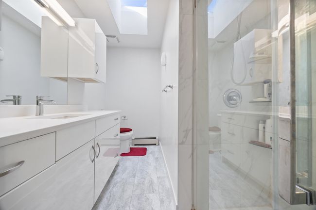 Bathroom featuring a shower stall, vanity, toilet, a skylight, and baseboard heating | Image 29