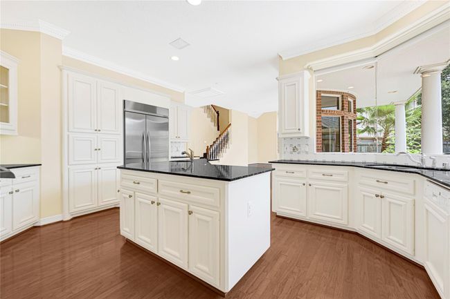 Discover a bright, spacious kitchen with elegant white cabinetry, granite countertops, and stainless-steel appliances. Enjoy a large central island and abundant natural light from expansive windows overlooking the patio and lush landscaping. | Image 17